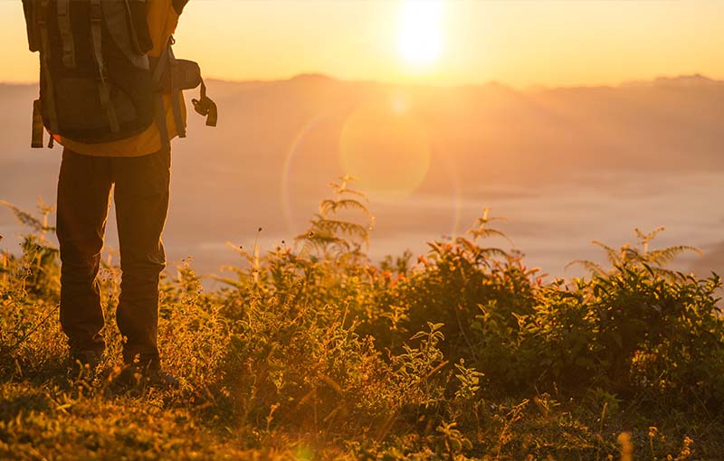 hiker-stand-camping-near-orange-tent-backpack-mountains